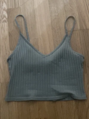Ribbad grön croppad linnetopp - Snygg grön ribbad linnetopp med smala axelband och v-ringning. Toppen är croppad och har en enkel, stilren design som passar perfekt till jeans eller kjol.