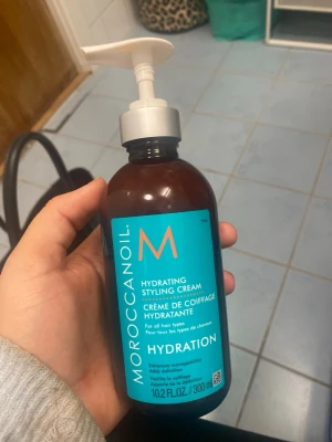 Moroccanoil Hydrating Styling Cream - OÖPPNAD!!!!!       Fuktgivande stylingkräm från Moroccanoil i en brun plastflaska med turkos etikett och vit pump. Passar alla hårtyper och hjälper till att mjukgöra och forma håret samtidigt som det ger glans och återfuktning. Innehåller 300 ml. 