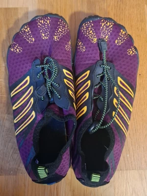 Lila fivefingers träningsskor - Unika träningsskor i lila med gula och svarta detaljer samt färgglad sula. Skorna har, snörning och ventilerande meshmaterial. Perfekta för barfotakänsla vid löpning eller gym. Snygg design med coola färginslag på sulan.