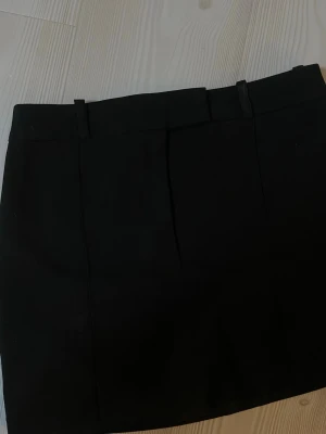 Svart kjol med bälteshällor - En stilren svart kjol med bälteshällor och diskret bakficka. Klassisk rak modell som är enkel att matcha till olika outfits. Perfekt för dig som gillar en clean och tidlös look.