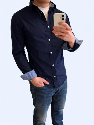 Mörkblå skjorta från Jack & Jones - Stilren mörkblå skjorta från Jack & Jones med vita knappar och klassisk krage. Skjortan har lång ärm och kontrastfärgade manschetter på insidan. Perfekt för en snygg och enkel look.