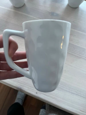 Vit mugg med kantigt handtag - Säljer 6st keramikmuggar med unik, kantig form på handtaget och lätt vågig yta. Muggen har en modern design och passar perfekt för kaffe eller te. Enkel och stilren look som funkar i de flesta kök.