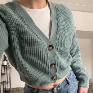 Blå/mintgrön ribbad kofta med knappar - Kort, ribbad kofta i ljusblått/mintgrönt med stora bruna knappar framtill. Koftan har v-ringning, breda muddar och en avslappna passform. Sitter bra och skönt men något urtvättad