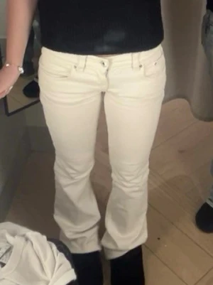 Vita bootcut jeans med detaljer - Säljer ett par vita bootcut jeans med snygga sömmar och små silvriga nitar på bakfickan. Jeansen har klassisk femficksmodell och låg midja. 