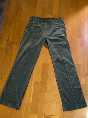 Mörkgröna äkta Juicy Couture byxor  - Mörkgröna mjukisbyxor i velour från Juicy Couture med raka ben och dragsko i midjan. Byxorna har fickor med dragkedja och en liten Juicy Couture-logga i strass på ena sidan. Perfekta för en chill och avslappnad stil. Jätte sköna och mjuka att ha på sig, det fanns logga på snörena men de har tyvärr gått av.