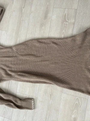 Beige stickad långklänning Adoore - Snygg beige stickad långklänning från Adoore med rund halsringning och långa ärmar. Klänningen har en figurnära passform och ribbade muddar vid ärmsluten. Perfekt för kyligare dagar och enkel att styla med boots eller sneakers.
