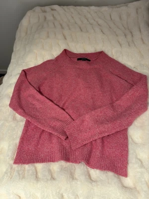 Rosa stickad tröja från Vero Moda - Mysig rosa stickad tröja från Vero Moda med rund halsringning och ribbade muddar vid ärmslut och nederkant. Tröjan har en avslappnad passform och är perfekt för kyliga dagar. Materialet är mjukt och bekvämt.