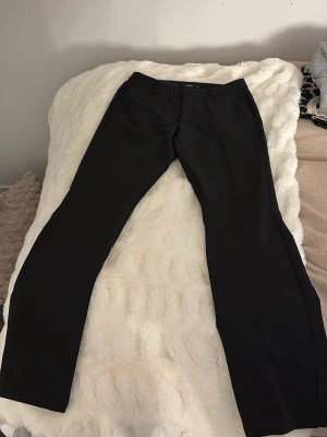 Svarta kostymbyxor från BikBok - Snygga svarta kostymbyxor från BikBok med klassisk rak passform. Byxorna har dragkedja och knapp framtill samt diskreta fickor. Perfekta för en stilren look och tillverkade i ett mjukt, vävt material som ger en bekväm känsla.