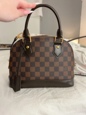 Alma BB  - OBS! Inte äkta. Säljer min jättefina ”Alma bb” väska, köpte den för 1800kr. Säljes pga att jag aldrig får någon användning för den längre, jättefina detaljer och alla märken sitter där de ska. Skriv för frågor! 💞Notera att i solljus ser lädret mer ljusare och slätare ut! :) alltså då perfekta färgen. 