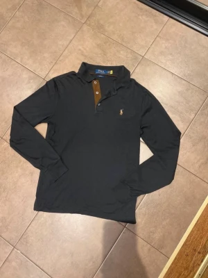 Svart långärmad piké från Polo Ralph Lauren - Svart långärmad piké från Polo Ralph Lauren med klassisk krage, riktigt cool logga på bröstet. Tillverkad i mjuk bomull som sitter snyggt och bekvämt. Perfekt för lyxig stil! Postar inom 24h📦 Köp mer än ett plagg för 10% rabatt!🤝