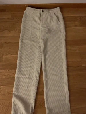Beiga raka manchesterbyxor - Säljer ett par beiga manchesterbyxor med raka ben och hög midja. Byxorna har klassiska fickor fram och bak samt stängs med knapp och dragkedja. Tillverkade i mjuk manchester som ger en retrovibe och passar perfekt till en avslappnad stil.