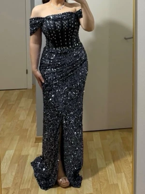 Glittrig svart långklänning offshoulder - Säljer en blå långklänning med glittriga paljetter och offshoulder-modell. Klänningen har en smickrande passform, markerad midja och slits framtill. Perfekt för dig som vill sticka ut med en elegant och glamorös look. Passar 38-40, klänningen är syd efter min kropp och önskemål. 