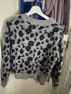 Grå leopardmönstrad stickad tröja XS - Säljer en grå stickad tröja från & Other Stories i storlek XS med svart leopardmönster. Tröjan har rund halsringning, långa ärmar och ribbade muddar vid ärmslut och nederkant. Perfekt för dig som gillar djurmönstrat och vill ha en trendig look. Den har blivit lite ”luddig” men inget man tänker på 