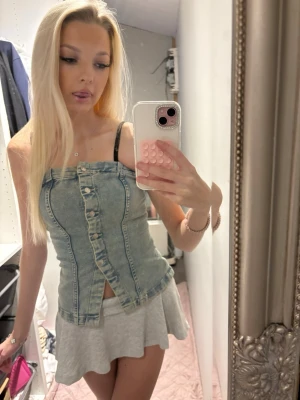 Denim tubtopp med knappar - Snygg tubtopp i ljusblå denim med knappar framtill och markerade sömmar. Toppen är axelbandslös och har en croppad passform som ger en cool och trendig look. Perfekt att styla med kjol eller jeans för en avslappnad vibe.