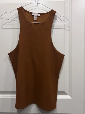 Brun ärmlös linnetopp från H&M - Snygg brun linnetopp från H&M med rund halsringning och minimalistisk design. Toppen är ärmlös och har en lätt strukturerad yta som ger en modern känsla. Perfekt att matcha med jeans eller kjol för en clean look.