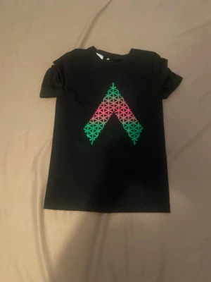Svart Adidas t-shirt med grafiskt tryck - Svart t-shirt från Adidas med ett stort grafiskt tryck i grönt och rosa på bröstet. Tillverkad i Climalite-material som andas och känns skönt mot huden. Perfekt för dig som gillar sportig och stilren design.
