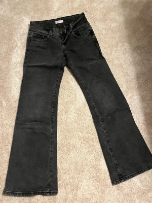 Svarta bootcut jeans från Perfect Jeans - Säljer ett par mörk grå bootcut jeans från Perfect Jeans. Jeansen har klassisk femficksmodell, dubbla knappar i midjan och dragkedja. Materialet är mjukt denim med lätt stretch och passformen är utsvängd nedtill. Perfekta för en trendig och avslappnad look.