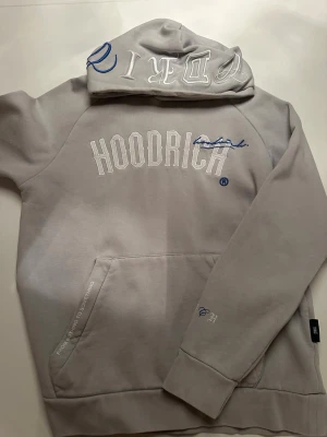 Grått Hoodrich loungewear set - Säljer ett grått loungewear set från Hoodrich med matchande hoodie och byxor. Setet har vita och blå detaljer, broderad HOODRICH-logga på både tröja och byxor samt fickor på båda plaggen. Perfekt för chill dagar hemma eller streetwear vibes.