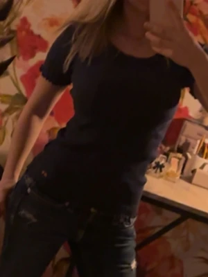 Mörkblå tight t-shirt - En enkel och stilren mörkblå t-shirt med rund hals och korta ärmar. Modellen är figurnära och passar perfekt till jeans eller kjol. T-shirten har en diskret liten logga vid höften och är tillverkad i mjukt bomullsmaterial.