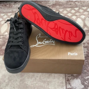 Intressekoll svarta Louboutin (äkta) - Snygga svarta sneakers från Christian Louboutin med klassisk röd sula och svarta skosnören. Skorna har en stilren design i mocka och läder, perfekt för dig som gillar exklusiva detaljer och streetstyle. Ikonisk logga på sulan och boxen medföljer ej finns defekter men inga större utifrån