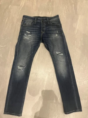Jack n jones jeans - Säljer ett par mörkblå jeans med slitningar och raka ben. Jeansen har klassisk femficksmodell och snygga slitdetaljer på låren och knäna. Perfekta för en avslappnad och trendig look.                     Nästan helt nya bara använda några gånger 29 30 