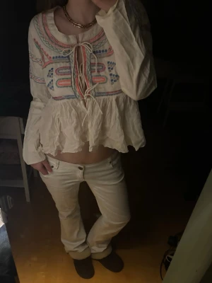 Vit boho-blus med brodyr och knytning - Superfin vit blus från ONLY med färgglad brodyr i blått, rött och grönt. Blusen har långa ärmar, volang nertill och snygg knytning framtill.
