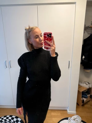 Svart stickad långärmad klänning - Svart stickad klänning med lång ärm och hög hals. Klänningen har en tight passform och en snygg slits på sidan som ger en cool touch. Perfekt för dig som gillar stilrena och bekväma plagg.