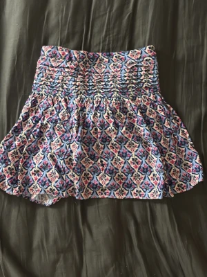 Blommig kortkjol från Zara - Supersöt kortkjol från Zara med blommigt mönster i blått, rosa och vitt. Kjolen har smock i midjan för en bekväm passform och är gjord i ett mjukt bomullstyg. Perfekt för dig som vill ha en färgglad och somrig look!