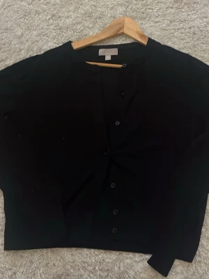 Svart cardigan från H&M - Svart cardigan från H&M med rund halsringning och knäppning framtill. Klassisk och enkel design med långa ärmar, perfekt att slänga över en t-shirt eller topp. Mjuk och bekväm, passar till många olika outfits.