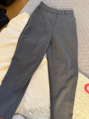 Grå kostymbyxor  - Snygga grå kostymbyxor från Amisu med raka ben och klassisk passform. Byxorna har hällor för skärp, diskret hake och dragkedja i midjan. Perfekta för en clean och stilren look. Materialet känns mjukt och har en lätt struktur.