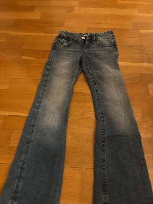Blå bootcut jeans med broderad ficka - Säljer ett par blå bootcut jeans från Miss Me med snygg slitning och broderad bakficka med paljettdetaljer. Klassisk femficksmodell och låg midja. Perfekta för dig som gillar en avslappnad men ändå trendig stil.