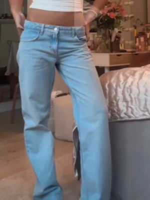 Jeans Zara - Säljer ett par ljusblå jeans med rak passform och klassisk femficksdesign. Jeansen har hög midja och stängs med knapp och dragkedja. Perfekta för en avslappnad och trendig look.