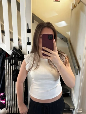 Vit ribbad topp med volangärmar - Snygg vit ribbad topp med volangdetaljer på ärmarna. Toppen har rund halsringning och är tillverkad i ett stretchigt material som sitter bekvämt. Perfekt att styla med jeans eller kjol för en fräsch look.💖