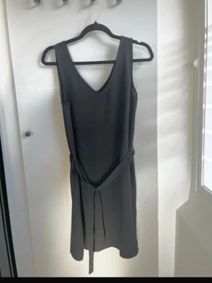 Svart klänning från Only - Säljer en svart kortklänning i rak modell med v-ringad hals och band i midjan. Materialet känns svalt, mjukt och följsamt.