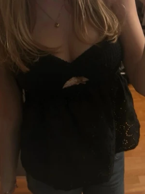 Svart spetslinnetopp med v-ringning - Snygg svart linnetopp med v-ringning och spetsdetaljer. Toppen är ärmlös och har ett litet hål under bysten för en extra touch. Perfekt att styla med jeans eller kjol för en trendig look.