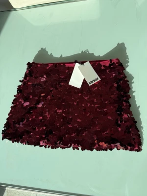 Vinröd paljettkjol från Bik Bok - Säljer en vinröd kortkjol från Bik Bok täckt med stora glittriga paljetter. Kjolen har en rak passform och är perfekt för dig som vill sticka ut. Supersnygg att styla med en enkel topp eller kavaj.