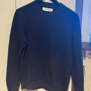 Mörkblå stickad tröja Samsoe Samsoe - Mörkblå stickad tröja från Samsoe Samsoe med rund halsringning och långa ärmar. Tröjan har en enkel, klassisk design med ribbstickade muddar vid ärmslut och nederkant. Perfekt för lager på lager och stilrena outfits.