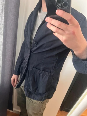 Mörkblå avslappnad kavaj - Snygg mörkblå kavaj från Morris med två stora framfickor och enkelknäppning. Modellen har en avslappnad passform och är tillverkad i ett lätt tyg, perfekt för en stilren look. Passar bra över t-shirt eller skjorta.