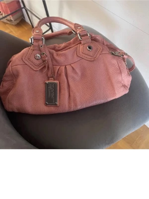 Ljus rosa marc jacobs väska - Säljer min super snygga marc jacobs väska i modellen classic Q pågrund av att den tyvärr inte kommer till användning. Den är i bra skick men har små täcken på användning. Fråga efter fler bilder!!
