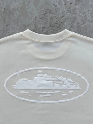 Corteiz | Alcatraz T-shirt - Vit t-shirt från Corteiz med ett diskret ton-i-ton tryck av ett landskap i oval form på både bröstet och ryggen. Klassisk rund hals och korta ärmar. Tillverkad i mjuk bomull för en skön känsla. Najs och lyxigt streetwear märke, hör av er vid minsta fundering 🤝