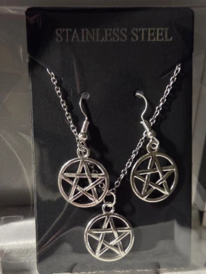 Smyckeset med pentagram i stål - Snyggt smyckeset i rostfritt stål med halsband och örhängen, alla med matchande pentagramhängen. Kedjan och krokarna är silverfärgade och designen är stilren och edgy, perfekt för dig som gillar alternativa accessoarer.