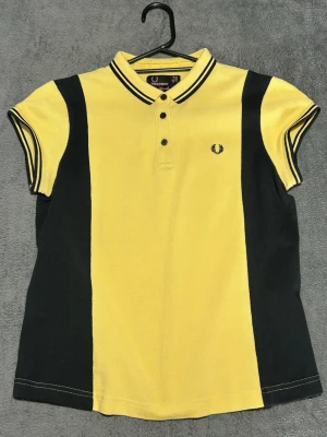 Fred Perry Polo Shirt – Yellow Black – Size S – Retro Style - Klassisk polo från Fred Perry i gul/svart design.  Riktig retro / mod vibe – sticker ut direkt.  Detaljer • Fred Perry • Kortärmad • Gul/svart panel design • Broderad logo • Storlek S  📦 Snabb frakt 💬 Hör av dig vid frågor