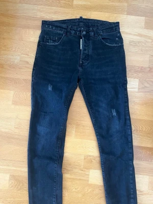 Svarta skinny jeans från Dsquared2 - Snygga svarta skinny jeans från Dsquared2 med diskreta slitningar och klassisk femficksmodell. Jeansen har en smal passform och detaljerad logotyp vid gylfen. Tillverkade i stretchigt denim för extra komfort och stil.