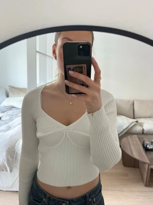 Vit ribbad topp - Säljer en vit ribbad topp med lång ärm och v-ringad urringning. Toppen har markerade sömmar under bysten för en snygg form och är stretchig. Super skön och endast använd fåtal gånger 