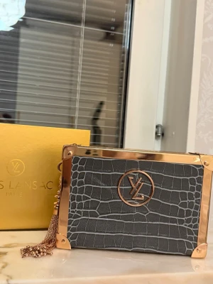 Grå kuvertväska från Yves Lansac - Snygg grå kuvertväska från Yves Lansac med krokodilpräglat mönster och detaljer i roséguld. Väskan har en axelkedja också. Aldrig använd 