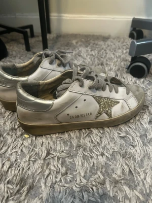 Golden Goose vita sneakers med glitterstjärna - Säljer ett par suupppersbygga sneakers i vitt läder med grå mockadetaljer och grå skosnören. Pris kan absolut diskuteras eftersom den vänstra skons sula är lite trasig (det kan lagas väldigt lätt med hjälp av lite lim) storlek 38 och jag säljer pga att dom inte kommer till användning längre❤️‍🔥❤️‍🔥❤️‍🔥