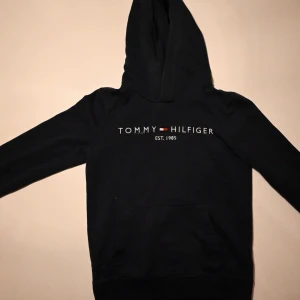 Tommy Hilfiger hoodie mörkblå - Snygg mörkblå hoodie från Tommy Hilfiger med klassisk logga på bröstet. Hoodien har en bekväm och avslappnad passform och passar perfekt till skolan. Perfekt för en avslappnad och trendig stil.
