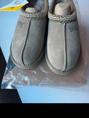 Beige UGG tofflor i mocka - Sprillans nya uggs, köpte dom i Australien men dom var för små och det märktes när jag inte längre va i Australien, därför inte returnerade. Alla tillbehör medföljer. 