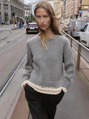 Grå stickad tröja med beige kant - Snygg grå stickad tröja med beige virkade detaljer längst ner och vid ärmsluten. Tröjan har en avslappnad passform, rund halsringning och långa ärmar. Perfekt för lager på lager och enkel att styla till olika outfits.