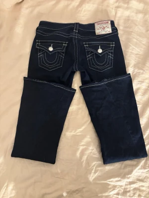 True Religion Jeans - Läs hela inlägget innan du klickar köp nu!  True Religion Joey Low Rise Jeans, säljes pga för korta i benen för mig (172cm). Använda ca. 3-4ggr så de är som nya, katt och hund finns i hemmet därav lite hår. 🐈‍⬛  Mörkblåa med vita sömmar och silvriga detaljer. Storlek: 24 Pris: 1000:- (Nypris: 1.299:-, Jeansbolaget Marieberg)  FÖRVARNING! ‼️ Gör inte samma misstag som mig! Jag köpte samma storlek som i light wash, de är perfekta i längd och midja, men dessa är mindre i storlekarna och töjs inte ut.